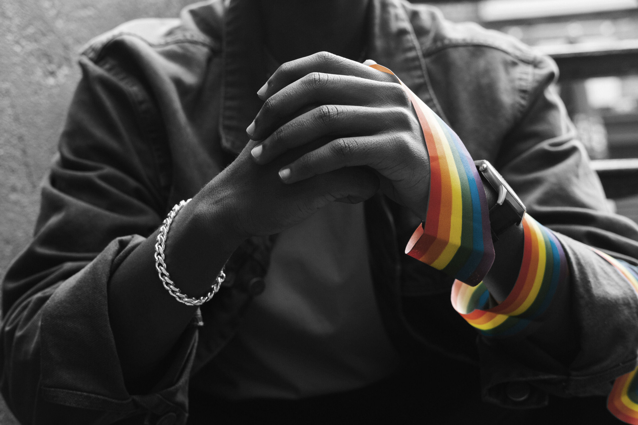 A cropped picture of a black man holding his hands with a rainbow pride ribbon wrapped around one wrist