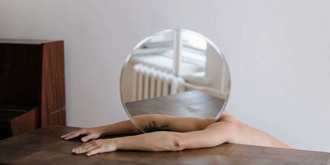 A man splayed out on a table with a round mirror by his head