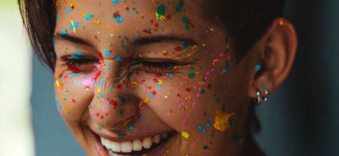 A girl smiling brightly with painted colors in her hair and speckled on her face