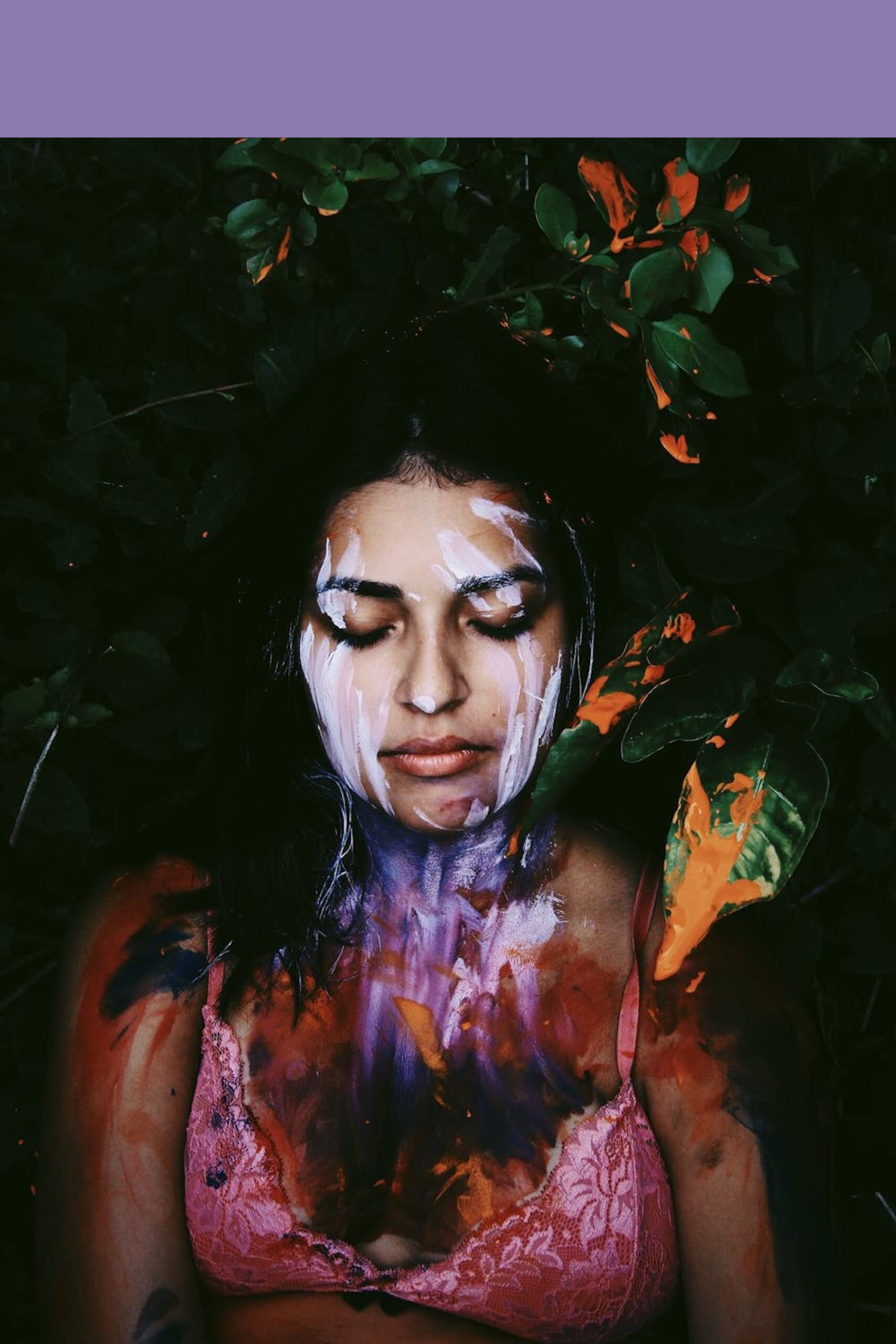 A meditative woman with paint on her body surrounded by plant leaves