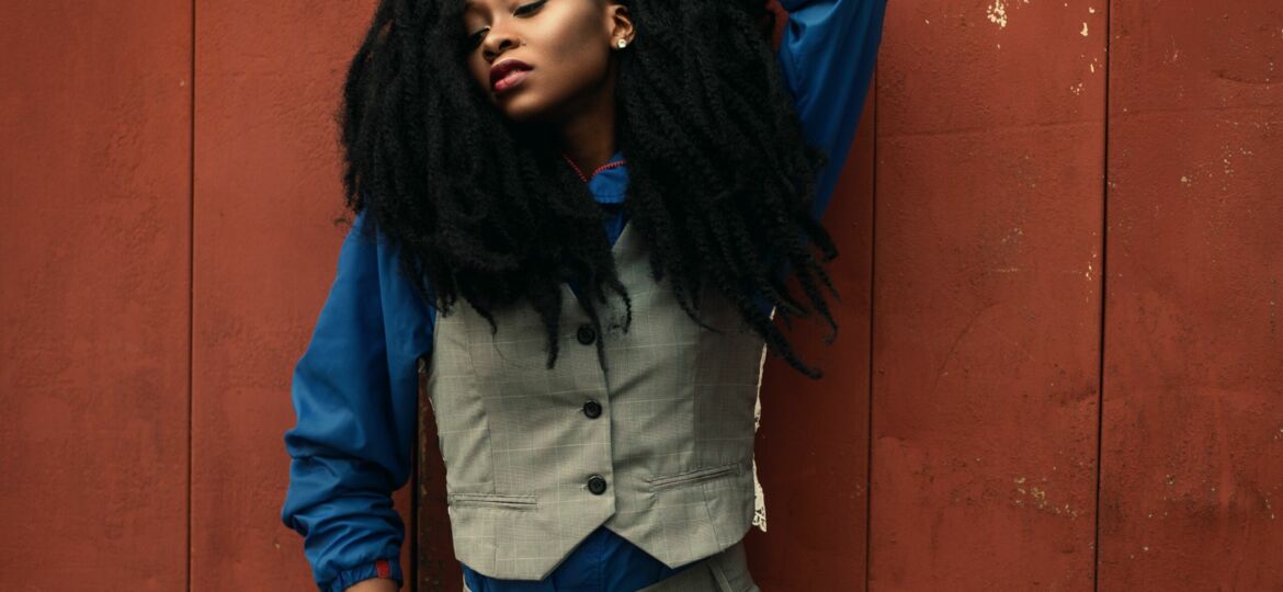 A black woman in a button down vest, pants and blue shirt with a full mane of hair